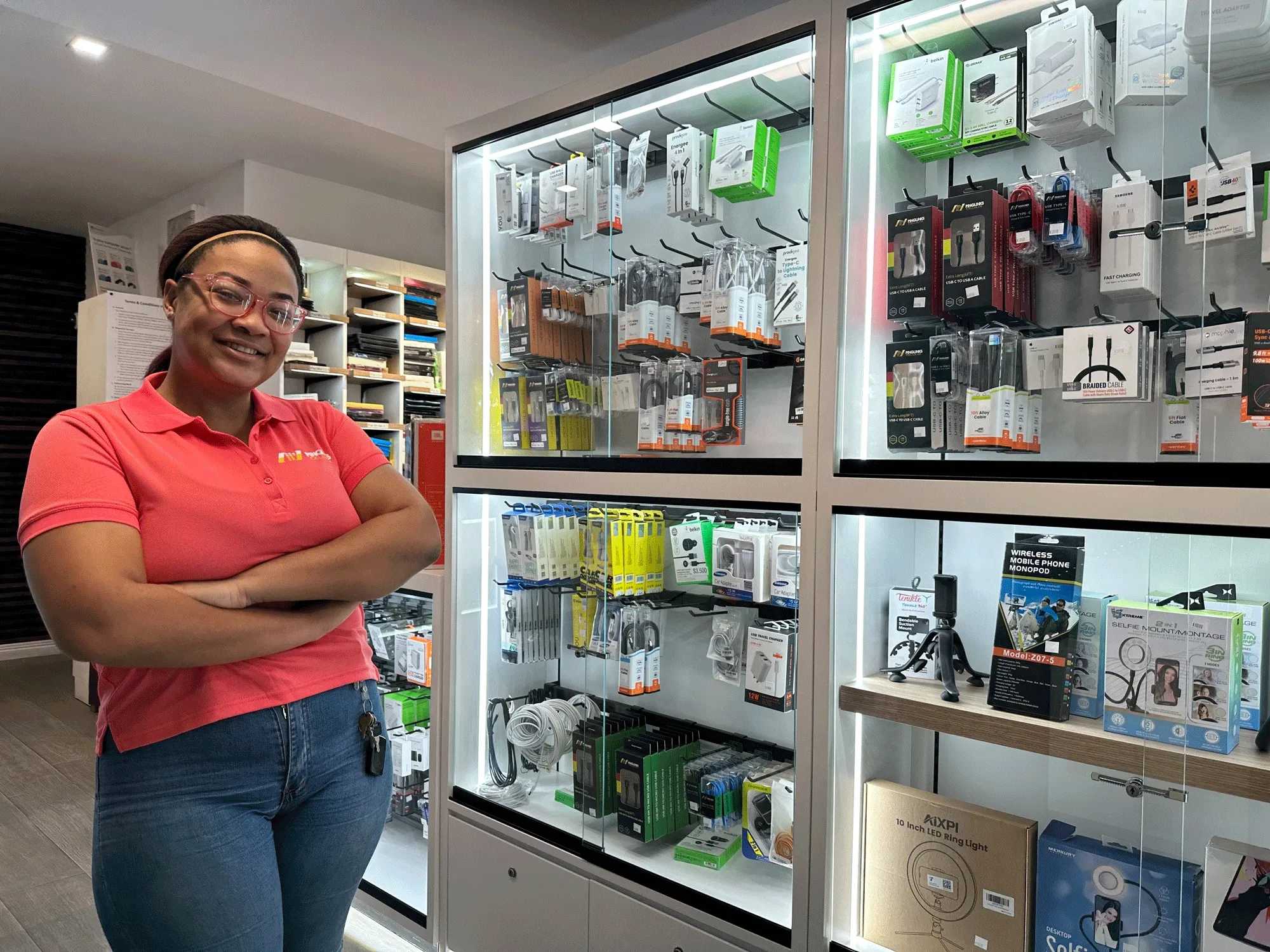 Pinglinks team member standing beside a lit wall display of phone chargers and cables